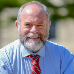 Headshot of a smiling bearded man with blue collard shirt and read tie